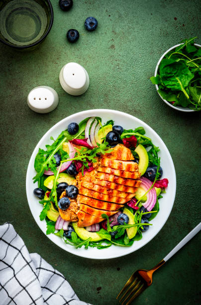 istock Green salad with grilled chicken, avocado and blueberries, rustic background, top view 2188126307