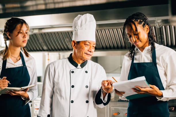 istock Professional Asian senior chef guides diverse students in a restaurant kitchen workshop. Focusing on teamwork learning and note-taking. Educational environment. Food Edocation 2188129143