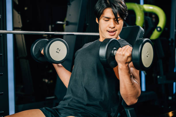 istock Asian man Muscular guy lifting dumbbell while sitting on bench gym, men using dumbbell during workout pumping up bicep muscle at fitness gym, workout healthy lifestyle 2188129200