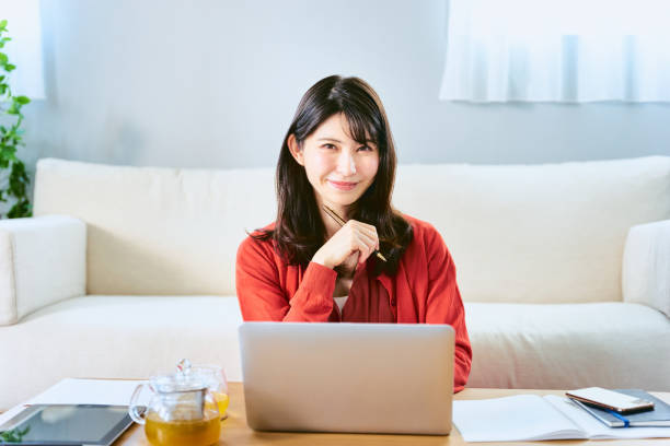 Spread materials, tablets and personal computers on the living room table, hold a pen, work and study a woman with a smile