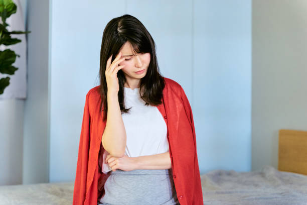 30代の日本人女性が、頭痛で座り込んで頭を抑えている - 月経前症候群 ストックフォトと画像
