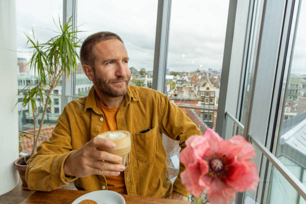A man enjoys a chai latte in a cafe with Amsterdam city view