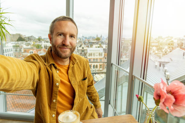 Man Taking Selfie While Enjoying Coffee in Modern Urban Apartment Near Large Window