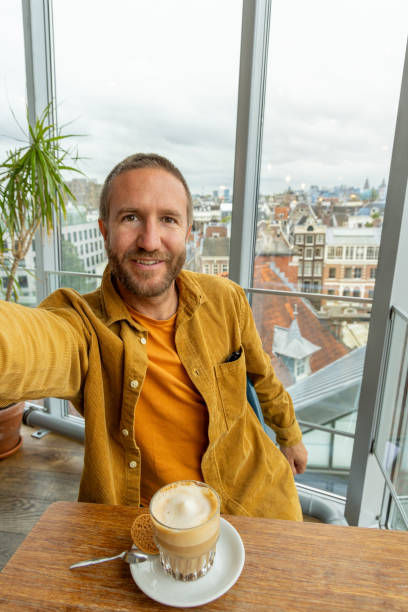 Man Taking Selfie While Enjoying Coffee in Modern Urban Apartment Near Large Window