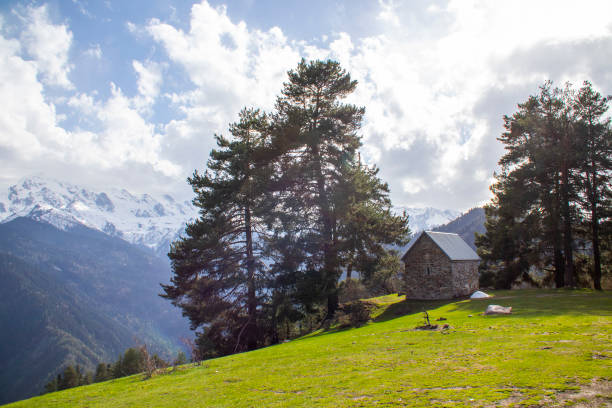A quaint little house is beautifully perched atop a lush, grassy hill in the serene mountains, surrounded by nature and tranquility