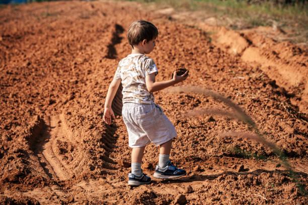 Little cute boy throwing stone in the dry field at summer day