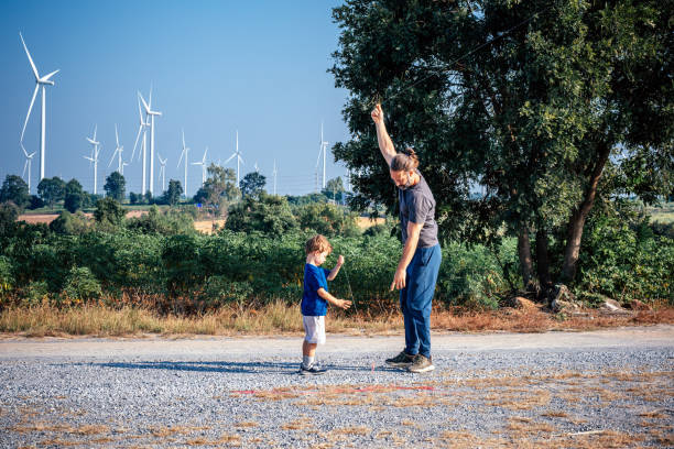Father is teaching his son how to fly a kite at wind farm