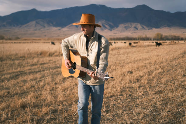 istock A shepherd is dancing in a field with a guitar in his hands. A man in a cowboy hat is playing guitar in a field. A musician is tending a herd of cows with a guitar in his hands 2188143473