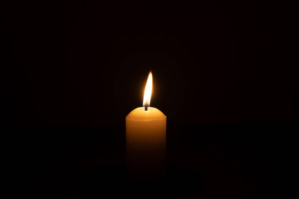 istock A single burning candle flame or light glowing on a big white candle isolated on black or dark background on table in church for Christmas, funeral or memorial service 2188145274