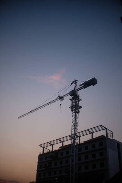 istock A construction crane towers over an unfinished building during twilight, silhouetted against a clear sky with subtle pink clouds. The scene conveys urban progress and industrial development. 2188159554