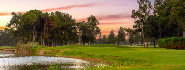 istock A tranquil golf course with a reflective pond and lush greenery, set against the soft pastel hues of a peaceful sunset. 2188163947
