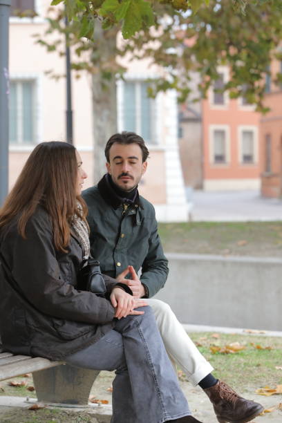 istock Young couple talking and gesturing while sitting on bench in urban park 2188168058