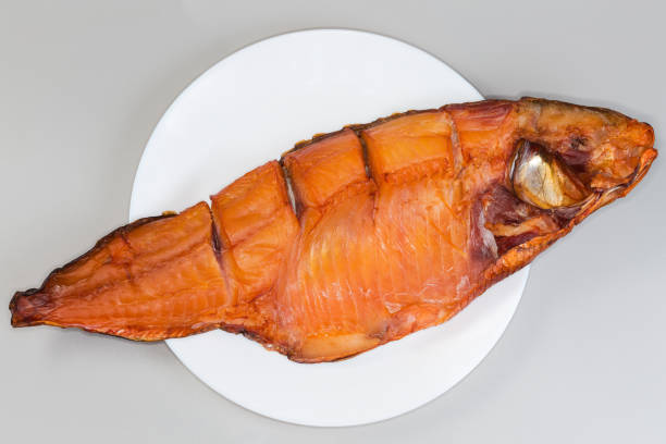 Grilled fish in a metal tray, surrounded by smoke, highlighting the culinary process of preparing seafood outdoors, evoking a sense of freshness and flavor