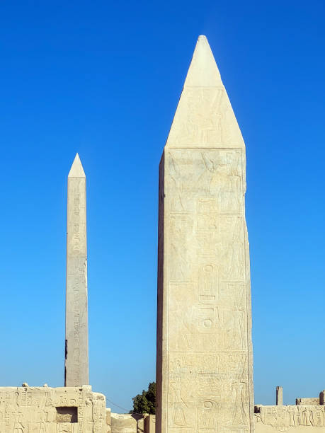 Two towering obelisks rise majestically at Karnak Temple, their ancient stone surfaces adorned with intricate carvings that tell the story of Egypt's rich history. Against a backdrop of a clear blue sky and bathed in the soft glow of the morning light, the obelisks stand as timeless symbols of Egyptian power and craftsmanship, their grandeur amplified by the serene atmosphere surrounding them.