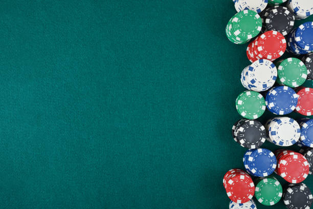 Detail of casino gaming background with stacks of betting chips of different colors to the right of the image on green gaming mat. Top view.