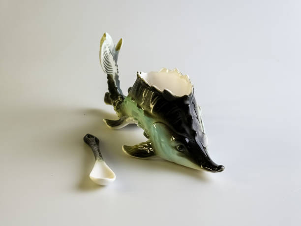 Caviar bowl with a spoon in the shape of a sturgeon on a white background. Specialized original dishes.