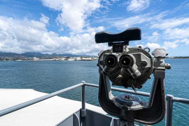 Vintage binoculars overlooking Pearl Harbor with a scenic view of the ocean and mountains under a partly cloudy sky.