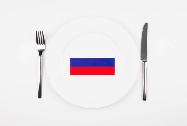 This conceptual photo showcases the Russian flag placed on a white plate, surrounded by a fork and knife, symbolizing Russian cuisine and culture. The minimalistic style emphasizes simplicity and elegance.