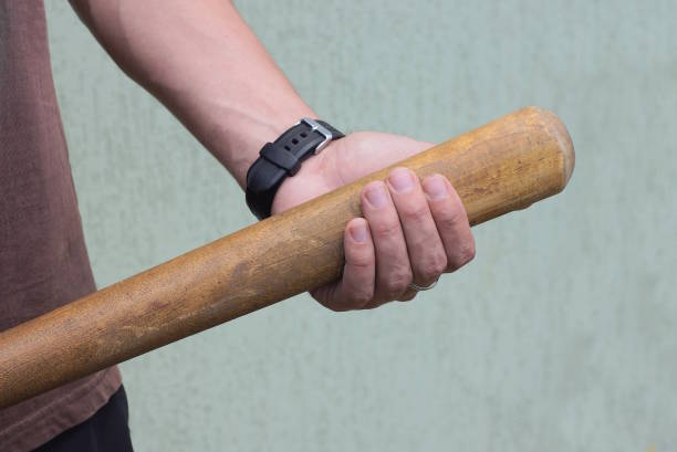 man hand holding one brown wooden bat near gray wall man hand holding one brown wooden bat near gray wall on summer street legs against the wall stock pictures, royalty-free photos & images