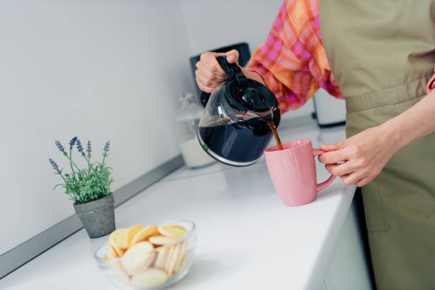 istock Charming woman in casual apron pours coffee into a pink mug while preparing breakfast in a bright kitchen 2188187174