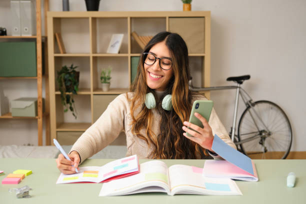 istock Young woman studying and taking notes while looking at smartphone at home 2188189839