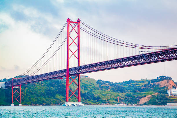istock Iconic Red Bridge Spanning Across Tranquil River Against Lush Green Hills and Cloudy Sky Captures Tranquility and Majestic Engineering of Coastal Region 2188191824