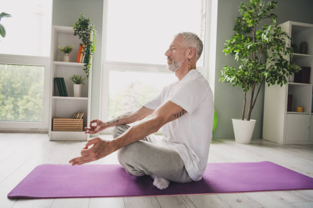 istock Elderly man practicing yoga on purple mat indoors, exhibiting serene and focused expression while wearing activewear 2188192318