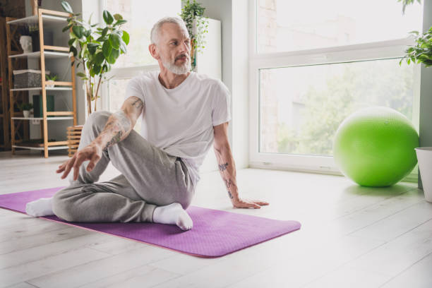 istock Elderly man practicing yoga on mat in bright room with natural light and green exercise ball nearby 2188192321