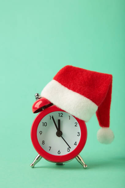 istock Red alarm clock with Christmas Santa hat on mint background. Vertical photo 2188207354