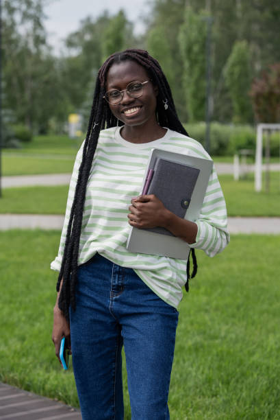 istock Smiling black student holding laptop and notebook in park 2188219874