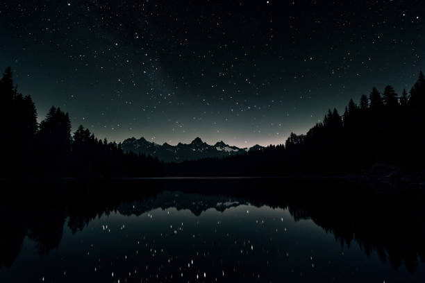Silhouette of mountains near lake on the huge full moon and night stars sky background.