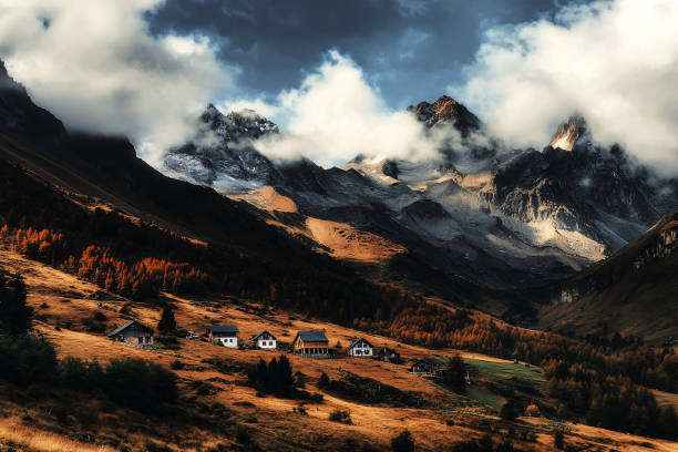 Nestled in the mountains, a small village basks in the golden light of dawn, with dramatic peaks towering above.