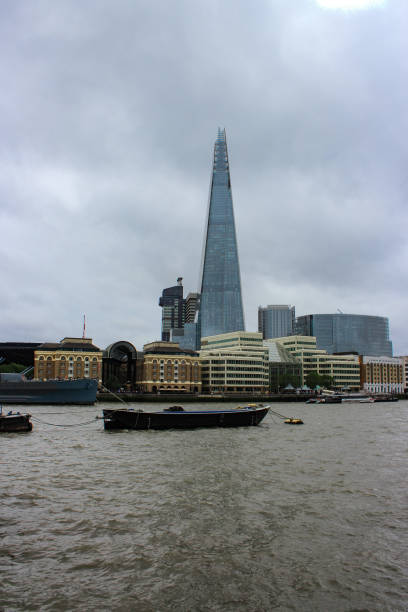 London, United Kingdom - Aug 4, 2023: The River Thames and the iconic shaped modern land mark building of the Shard London seen on a grey rainy day. A boat on the water.