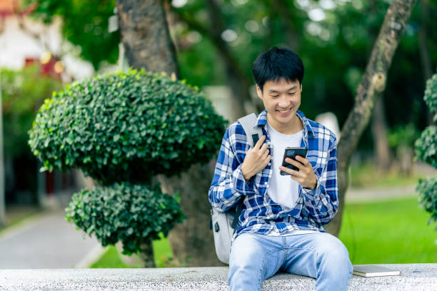 istock Asian male university student holds a smartphone, searches information on the internet, talks with friends, does outdoor activities. 2188226758