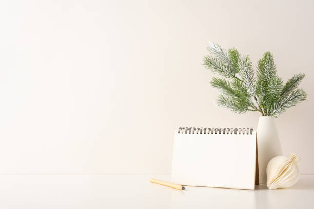 A side view minimalist Scandinavian-style workspace with a blank notebook, pine branch decor in a vase, and pencil. Ideal for conveying simplicity and winter themes