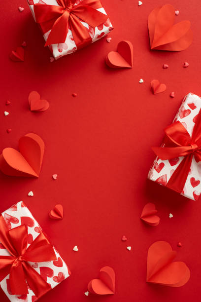A vertical visually striking Valentine's Day arrangement featuring beautifully wrapped gifts and vibrant red paper hearts, creating a romantic and festive atmosphere