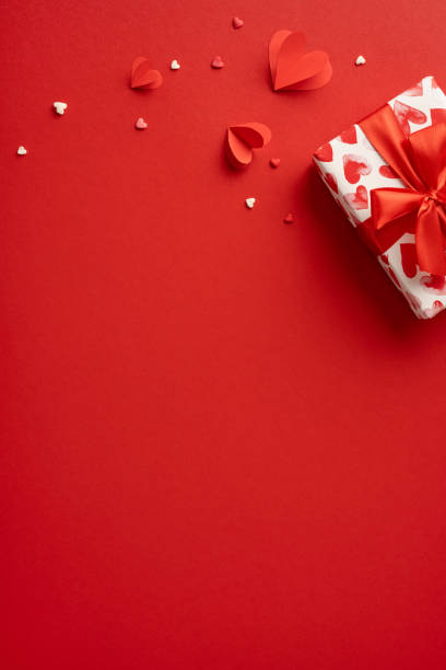 istock A vertical beautifully wrapped gift box with red ribbon sits on a vibrant red background adorned with paper and candy hearts, perfect for a romantic Valentine's Day celebration 2188236026