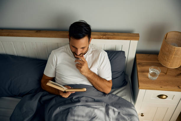 istock Above view of a man reading book in bed. 2188240246