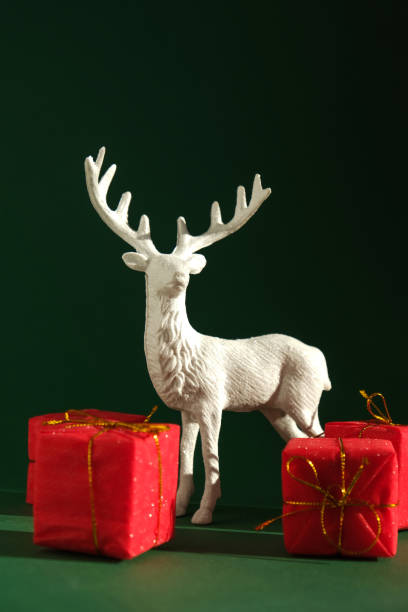istock Festive composition with an elegant figure of a reindeer surrounded by bright red gift boxes on a rich green background. 2188240927