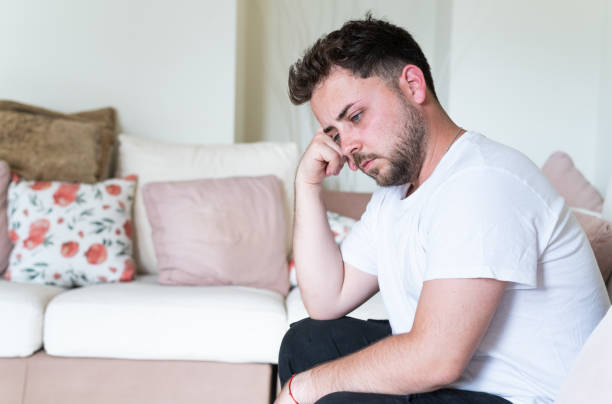 istock Young man feeling depressed at home sitting on floor by sofa 2188243837