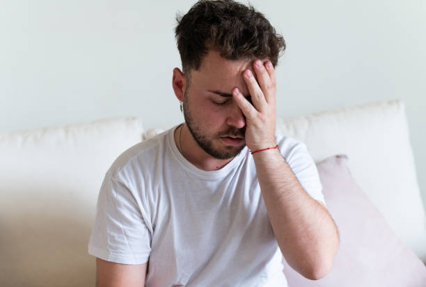 istock Young man suffering from headache sitting on bed covering face 2188243866