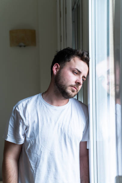 istock Young man suffering from depression leaning against window 2188243868