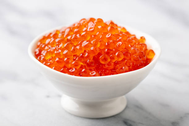istock Red salmon caviar in white bowl. White marble background. Close up. 2188247706