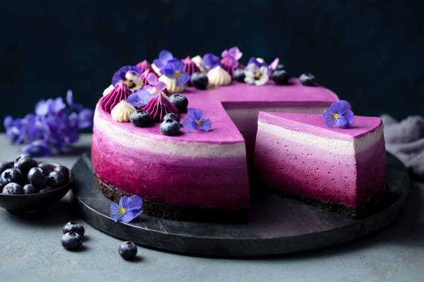 Blueberry violet mousse cake, no bake cheesecake with edible flowers on marble board. Dark background. Close up.