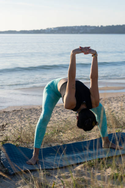 istock Young woman practicing wide-legged forward bend yoga pose on a beach mat at sunrise, embracing the tranquil ocean view 2188253751