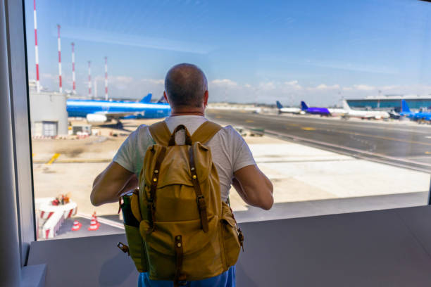 istock Rear view of man with backpack looking through window on airport runway 2188255604