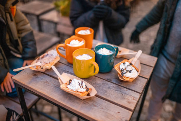 A cozy outdoor setting features steaming mugs and delicious waffles topped with cream, symbolizing a joyous gathering.