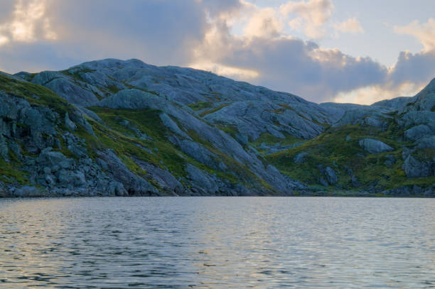 istock A serene lake surrounded by rugged, grassy hills and rocky terrain under a cloudy sky. 2188266270