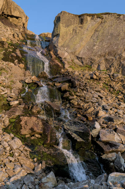 istock This image captures a serene rocky waterfall illuminated by the warm hues of sunset light. 2188266271
