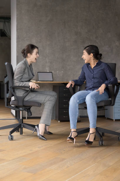 istock Two laughing women laughing seated on chairs at workplace 2188277909